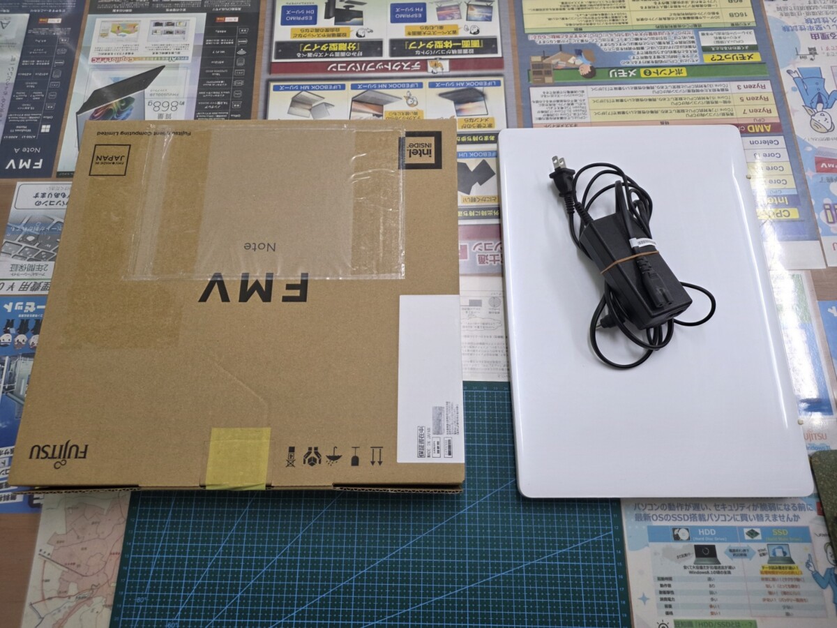 未開封のFMV Noteの箱と、白いACアダプター・電源ケーブルを上から確認している様子