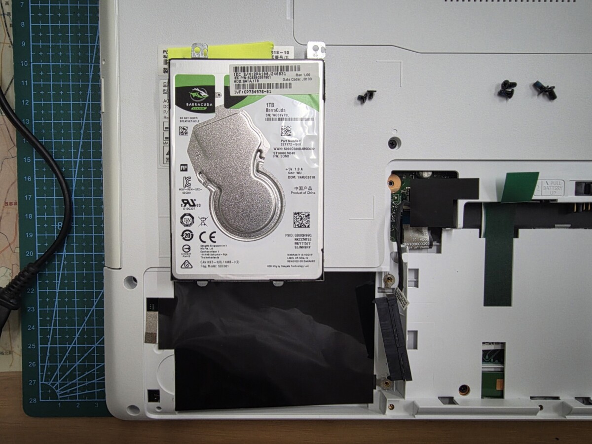 パソコン本体から取り出された2.5インチのSeagate BarraCuda 1TBハードディスク。周囲にネジが並べられている
